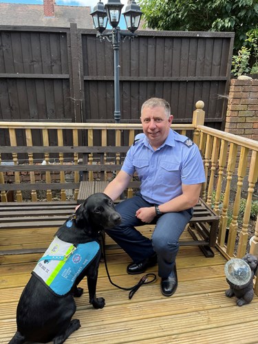 Royal Air Force personnel Dan Milward in uniform sat outside on a bench with assistance dog Aldo who has his dog jacket on